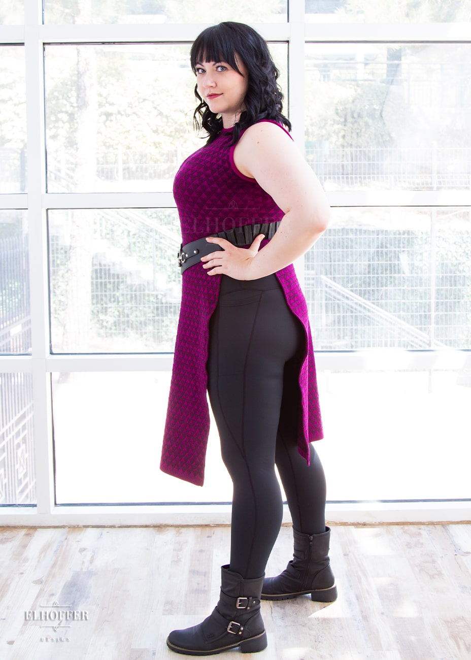 Bernadette, a fair skinned size large model with short black hair and bangs, is wearing a pullover cropped sleeveless knit top with front and back flaps in a magenta triangle knit.