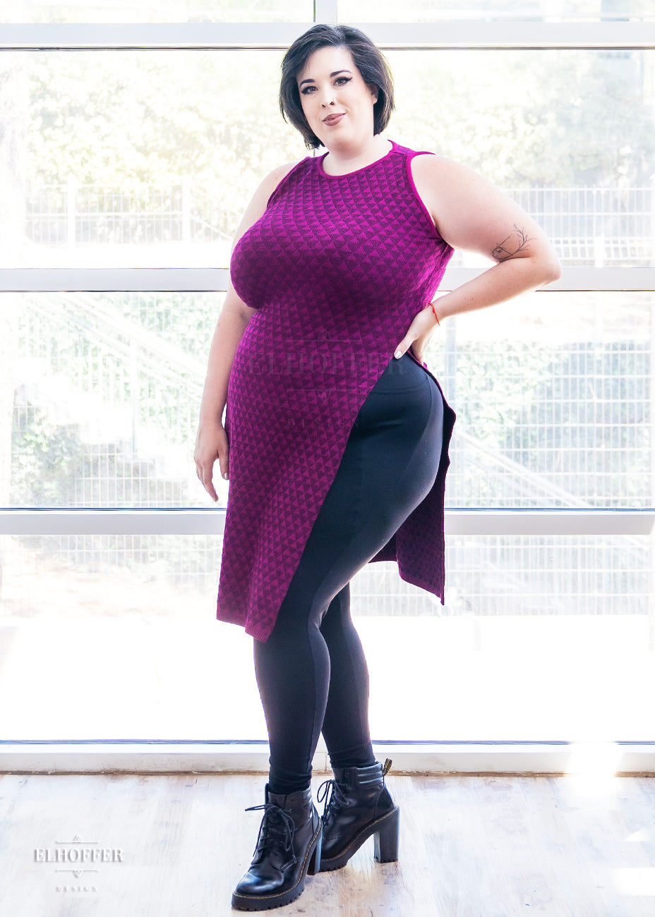 Katie Lynn, a fair skinned size 2XL model with short black hair, is wearing a pullover cropped sleeveless knit top with front and back flaps in a magenta triangle knit.