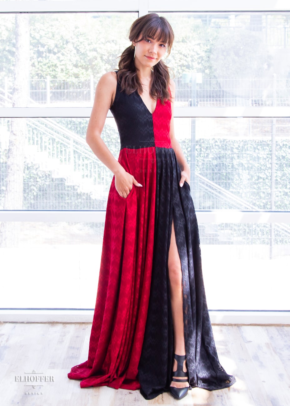 Erika, a size XS model with olive skin and long light brown hair, is wearing our Queen of Hearts Sirens Gala Gown. It is a pullover dress with low v-neck and side pockets with an incredibly full skirt with high slit covered in lace. One half of the top is red, one black, and the skirt is the opposite colors.