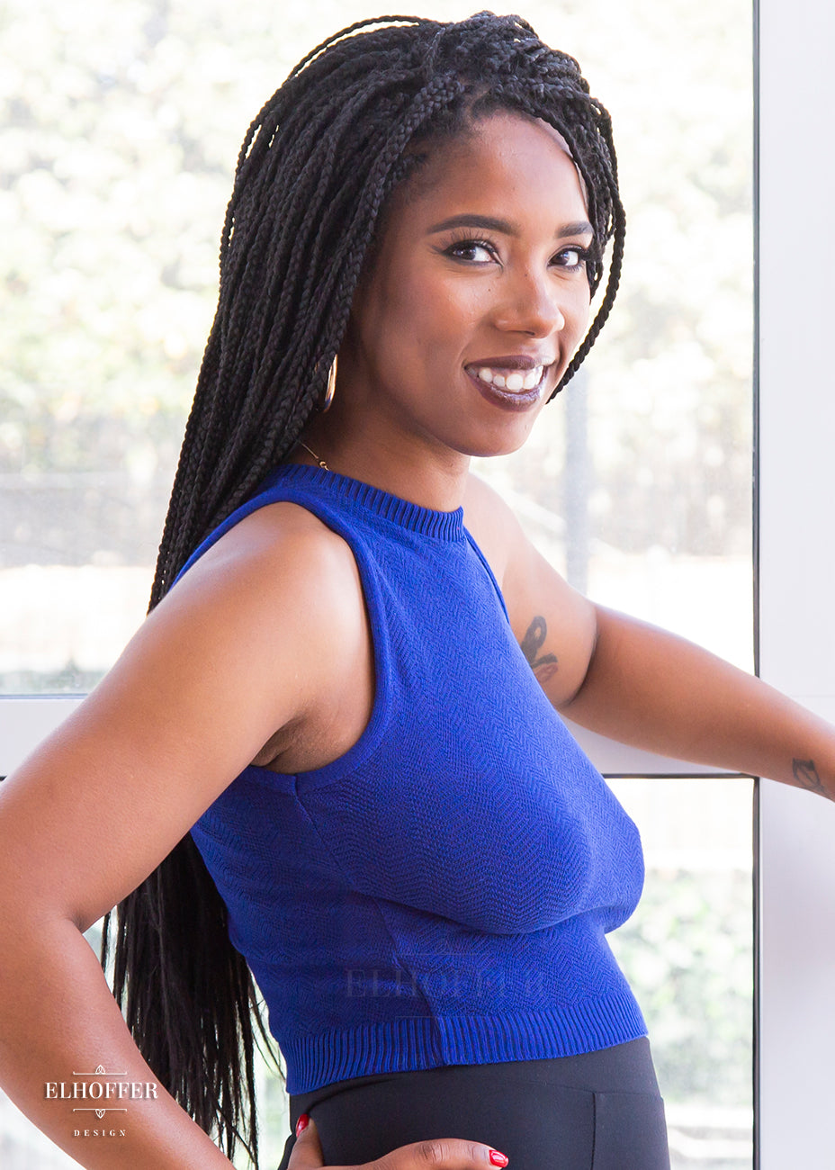 Krystina, a size small medium dark skinned model with long dark braids, shows off the size profile of the royal blue knit top.
