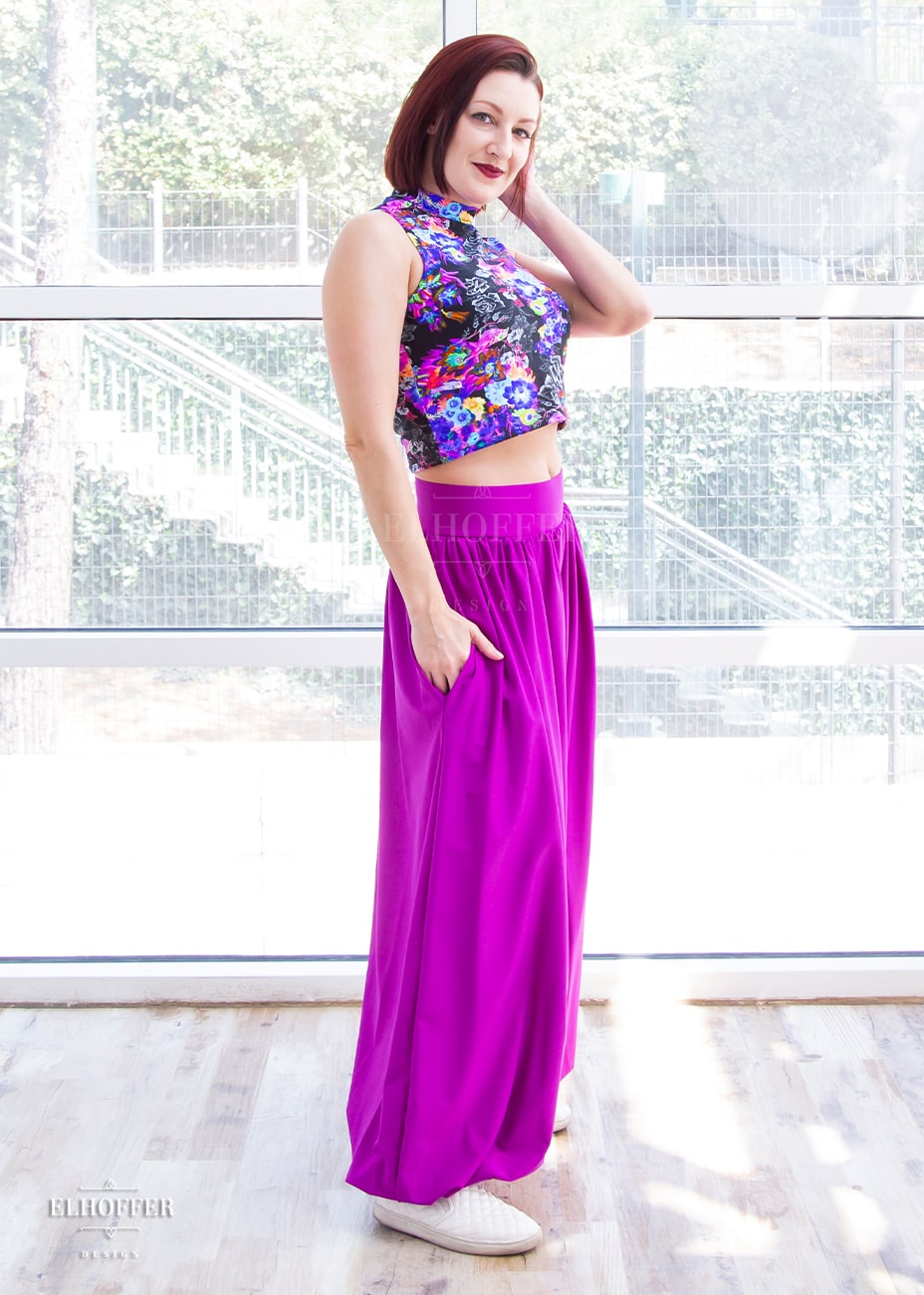 Natalie, a size small fair skinned model with short red hair, is wearing bright magenta high waisted full pants gathered at the waist and ankle with a drop crotch seam and side pockets.
