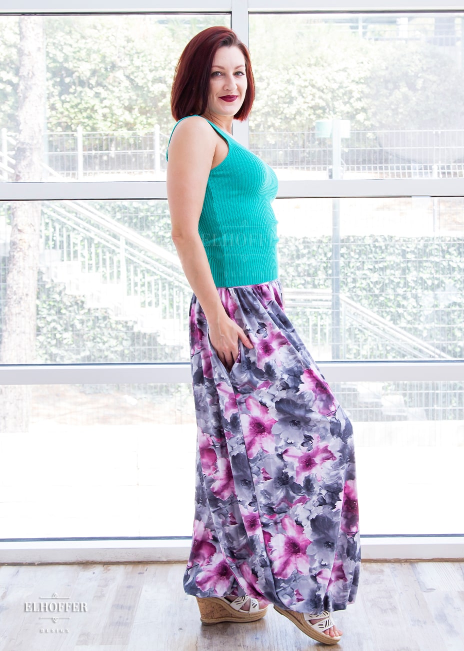 Natalie, a size small fair skinned model with short red hair, is wearing our essential Yasmin pants in the watercolor flowers print. The pants are high waisted full pants gathered at the waist and ankle with a dropped crotch seam. The watercolor flowers print is greyish purple, pink, and white, and gives the impression of a water color painting.