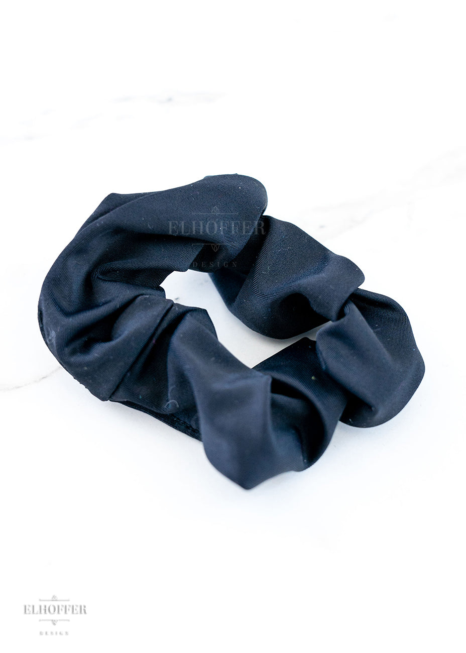 A solid black scrunchie on a marbled white background.