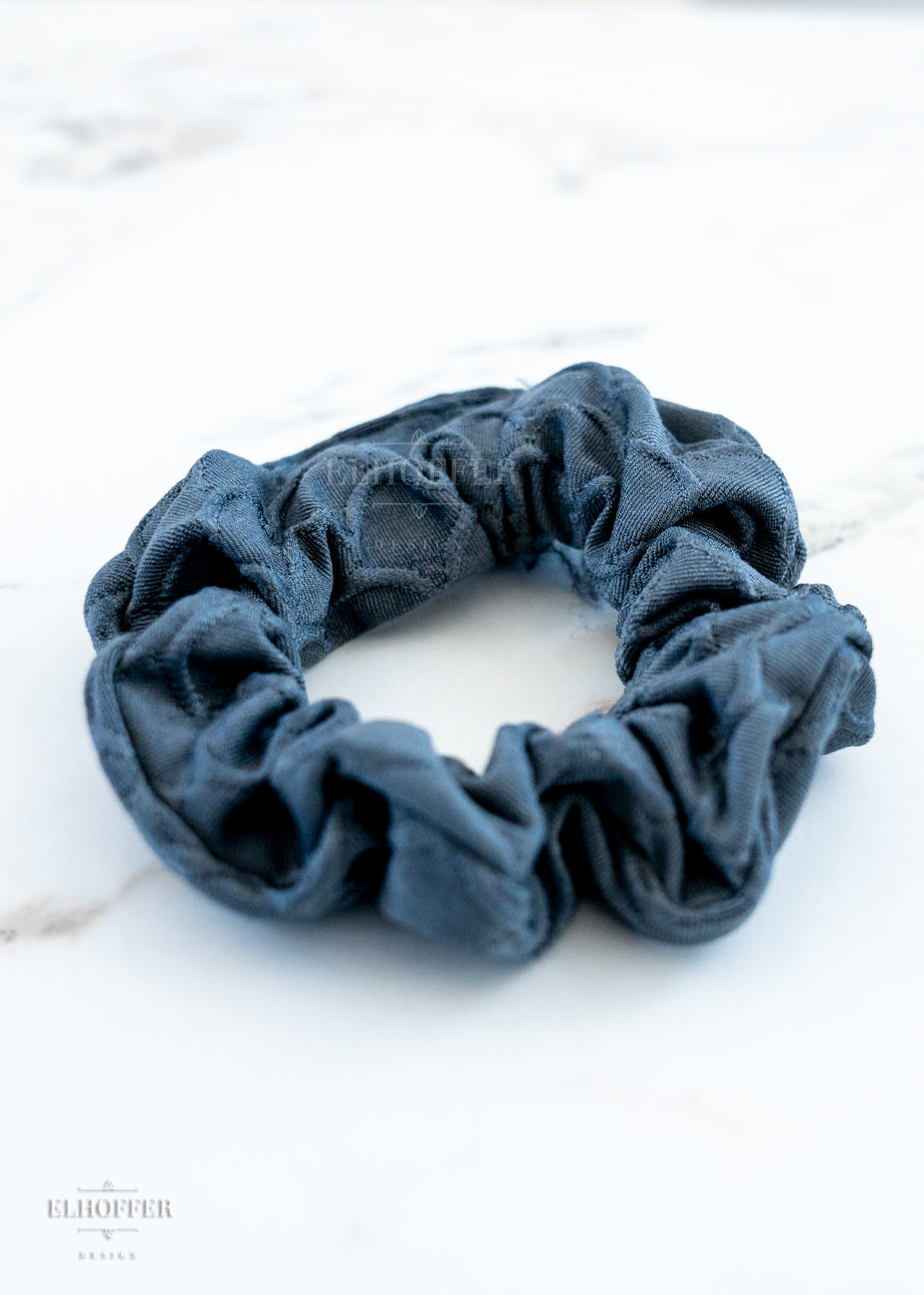 A grey scale textured scrunchie on a white marbled background.