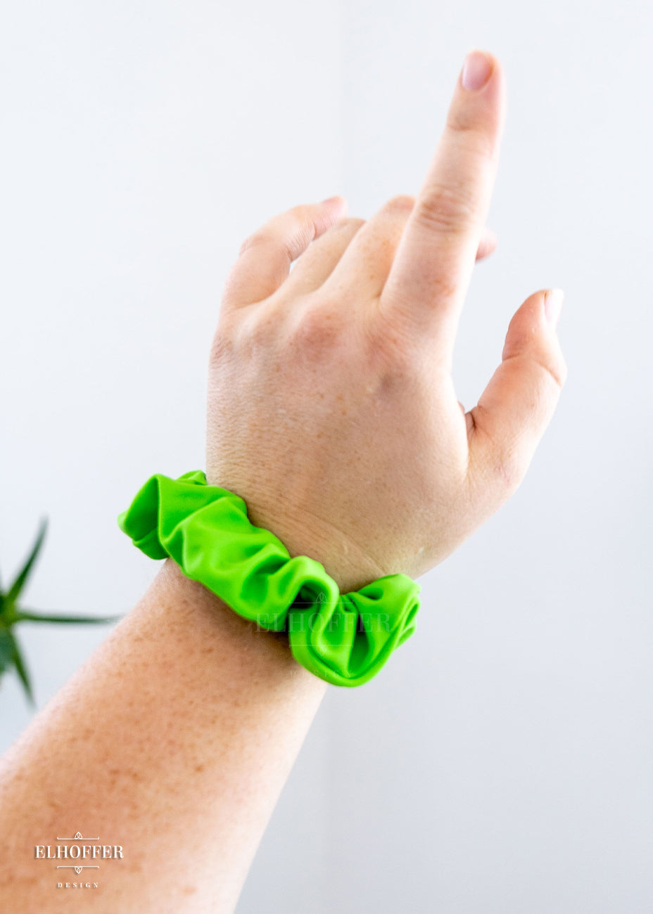 A fair freckled arm wearing a bright green scrunchie. 