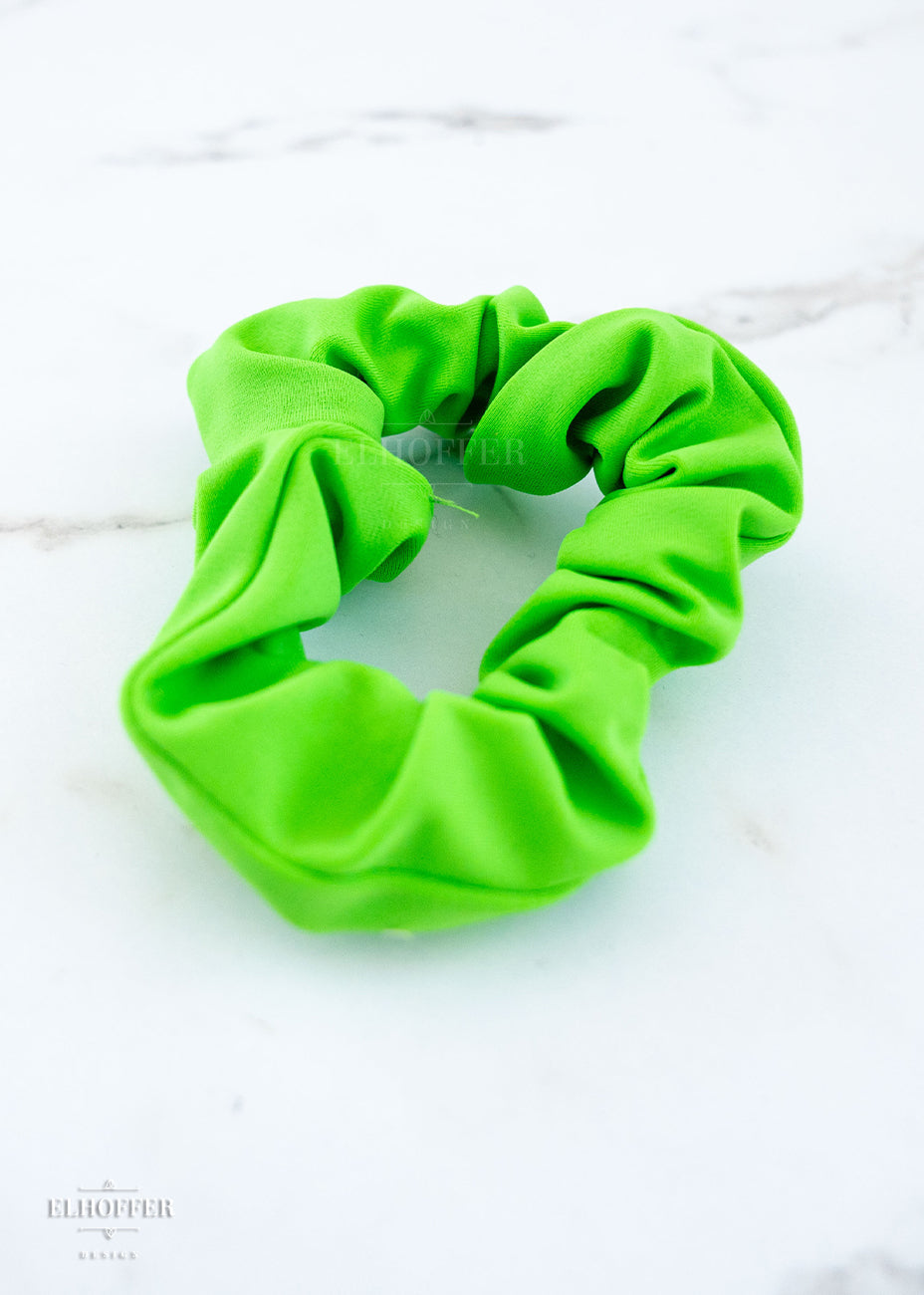 A bright green scrunchie on a white marbled background.