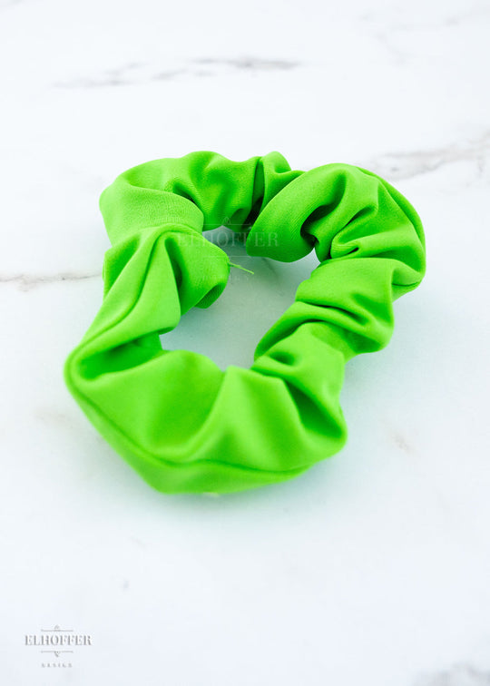 A bright green scrunchie on a white marbled background.