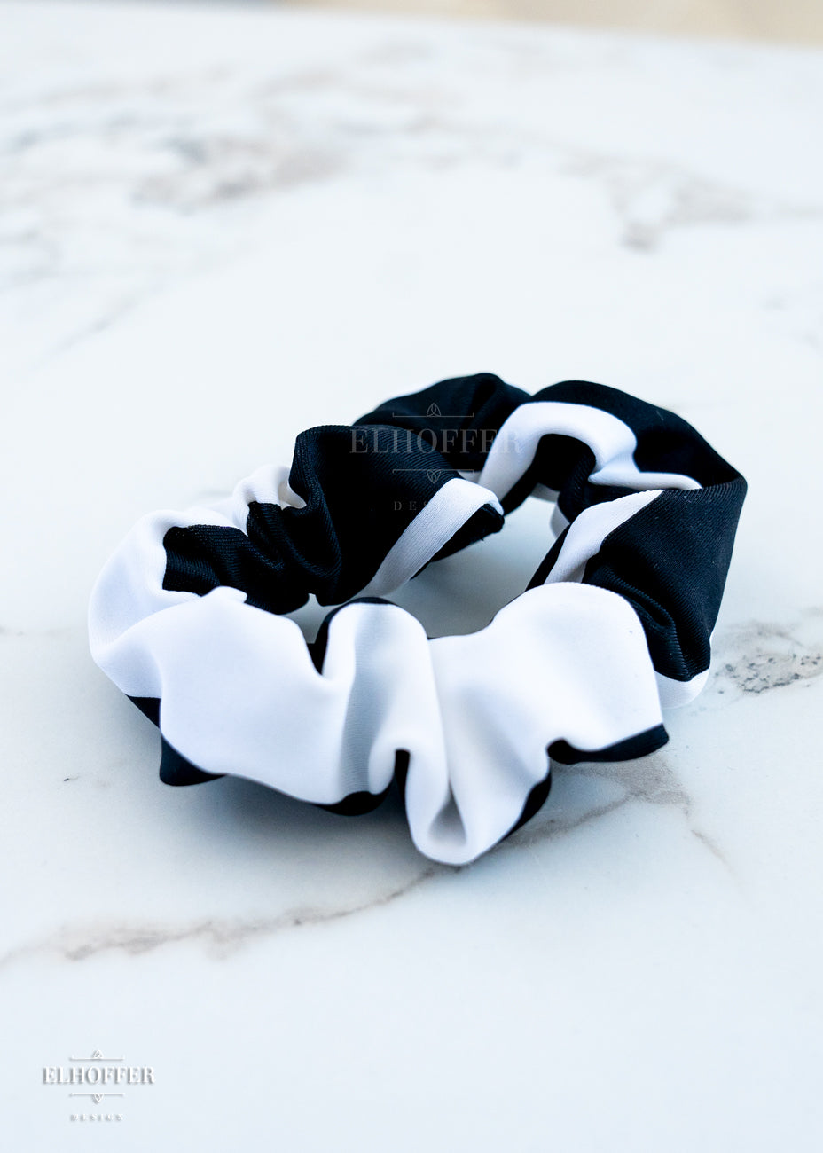 A black and white striped scrunchie laying on a white marbled background.