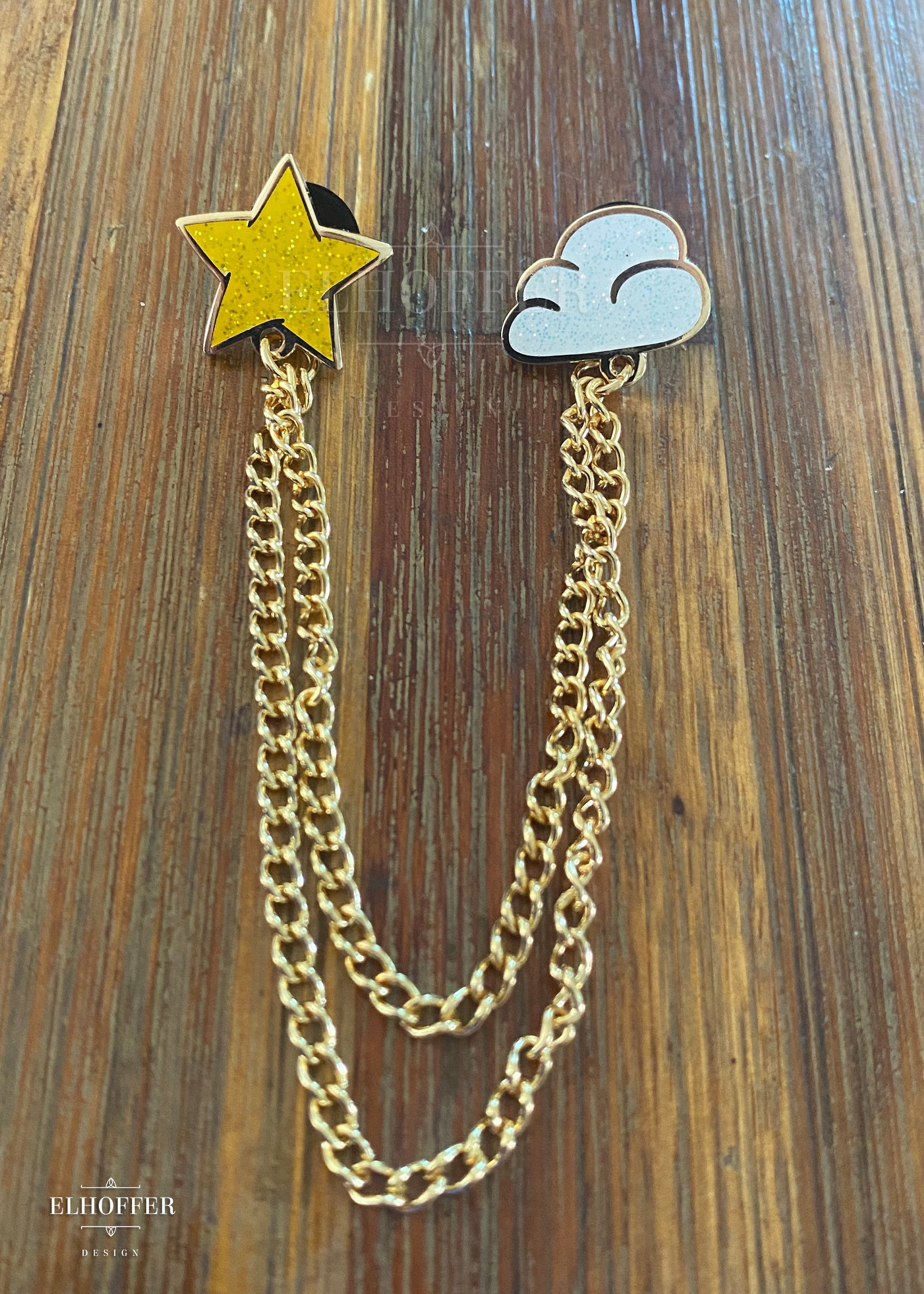 A tiny star pin and a tiny cloud pin connected together with 2 lengths of gold chain.